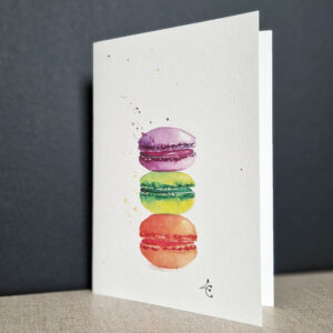 Dessin d'un macaron délicatement peint à l'aquarelle sur une carte d'art, mettant en valeur ses couleurs pastel et sa texture fondante
